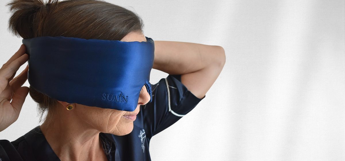 Woman adjusting a deep blue Still Suain silk sleep mask