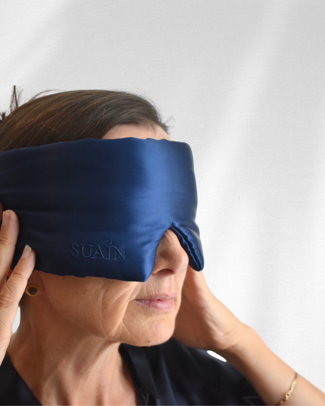 Woman adjusting a deep blue Still Suain silk sleep mask