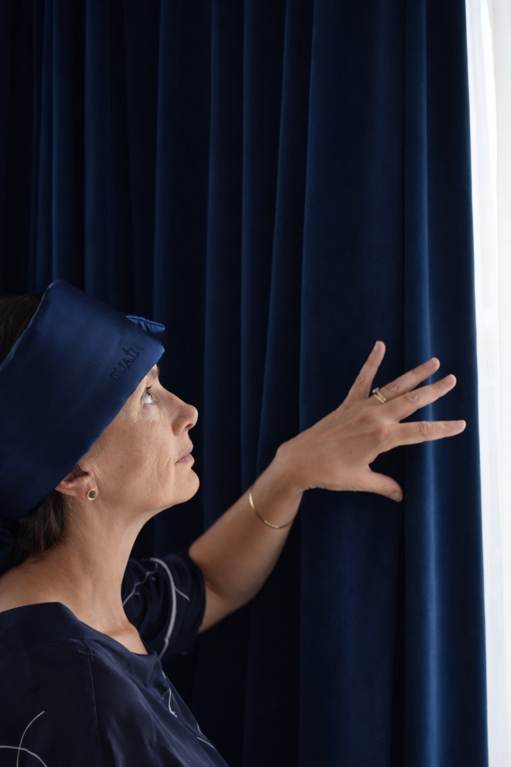 Woman in white sleepwear touching rust-coloured velvet curtains